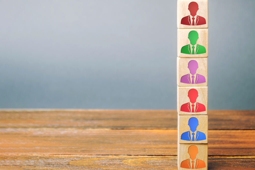 Seis bloques de madera apilados con siluetas de directivos en distintos colores, representando los diferentes tipos de liderazgo en una empresa.