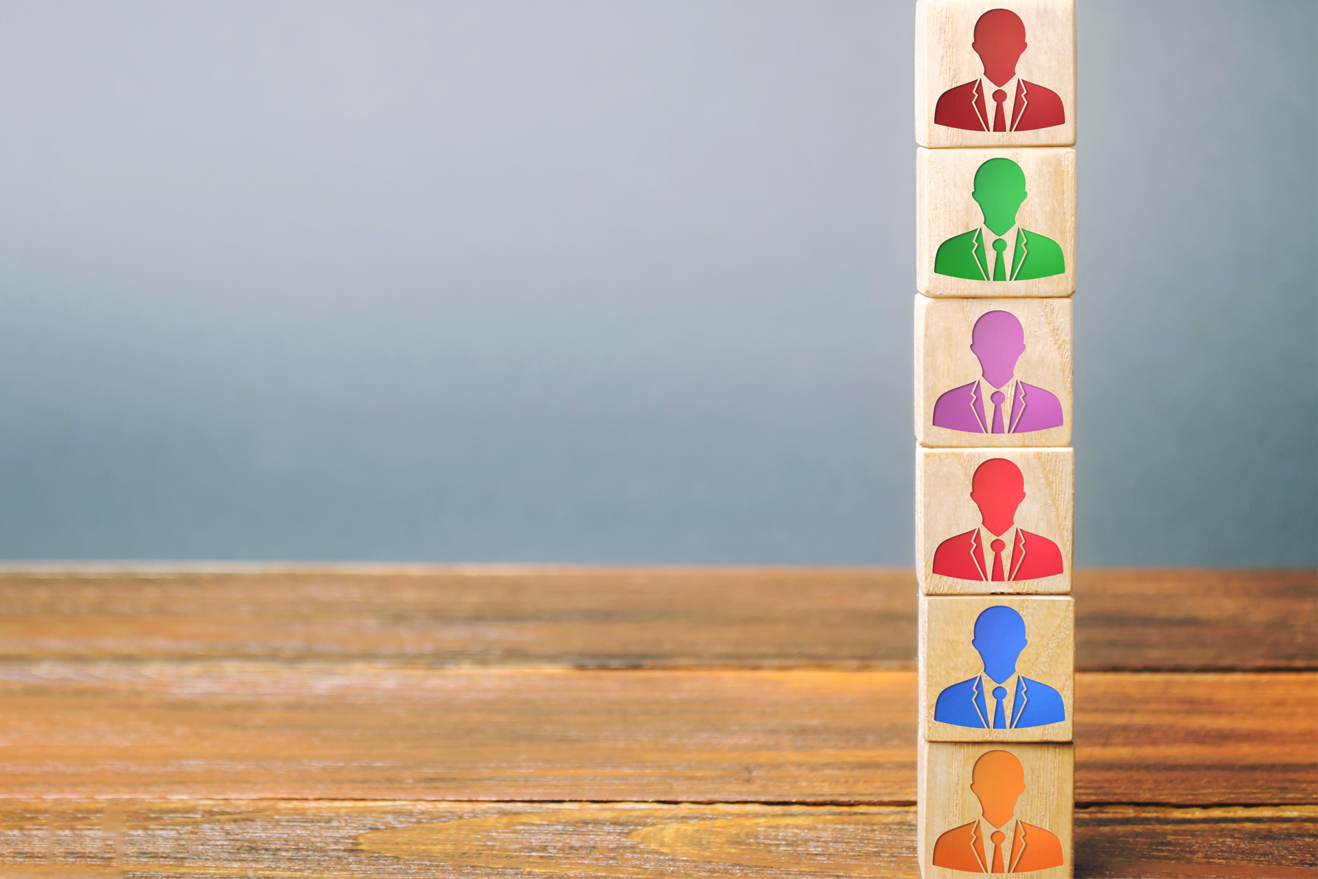 Seis bloques de madera apilados con siluetas de directivos en distintos colores, representando los diferentes tipos de liderazgo en una empresa.