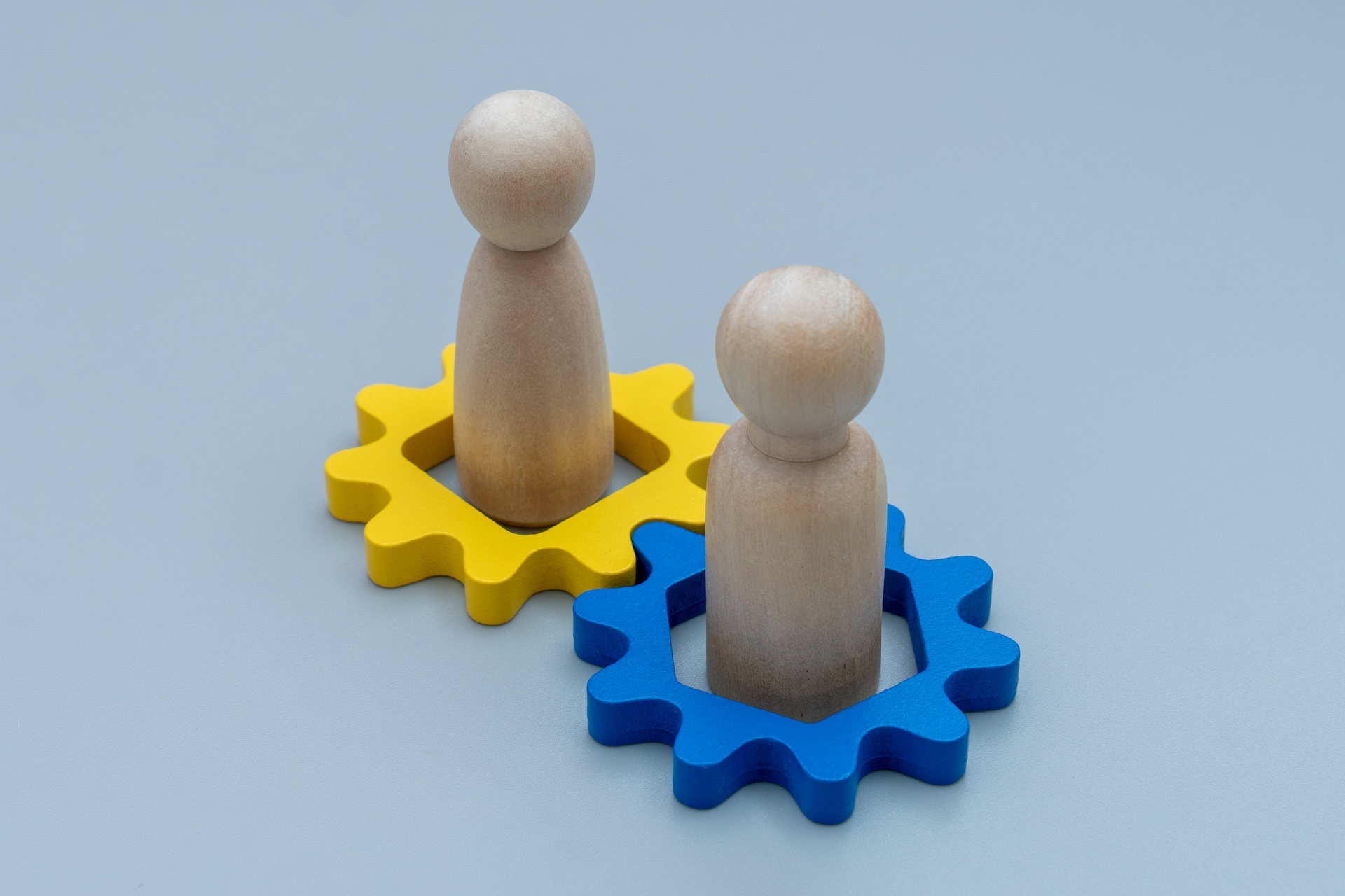Dos muñecos de madera minimalistas de FORESVI en engranajes de color amarillo y azul marino, simbolizando el encaje estratégico del equipo con la disc prueba psicotécnica.