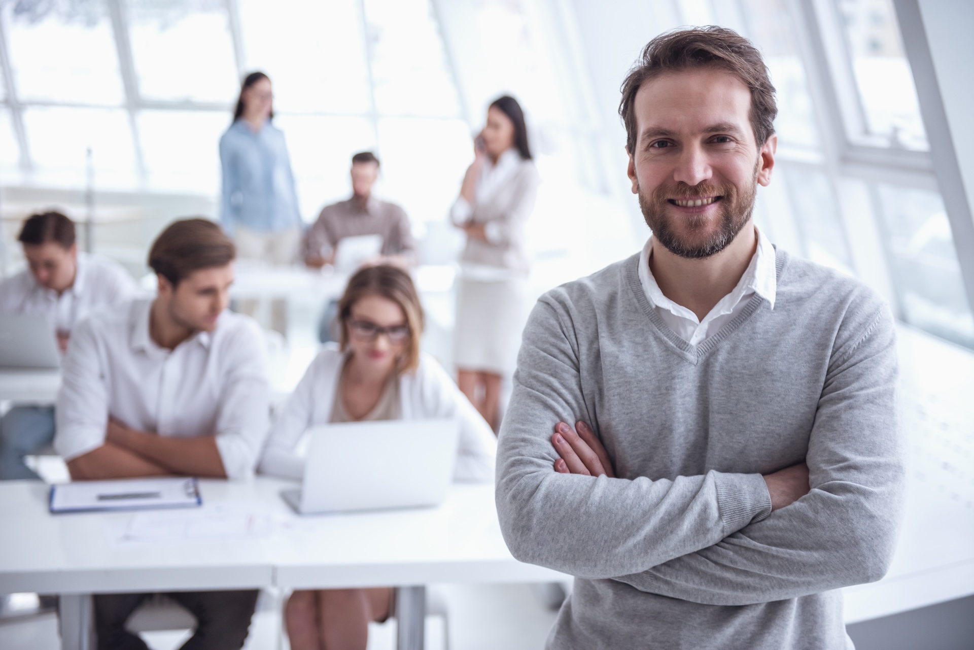 Gerente de pyme relajado y sonriente en primer plano mientras su equipo trabaja de forma autónoma al fondo, fruto de la mentorización empresarial.